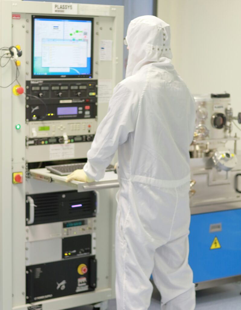 Naukowiec w białym kombinezonie ochronnym przy aparaturze laboratoryjnej, prowadzący badania nad nanosrebrem i nanotechnologią.